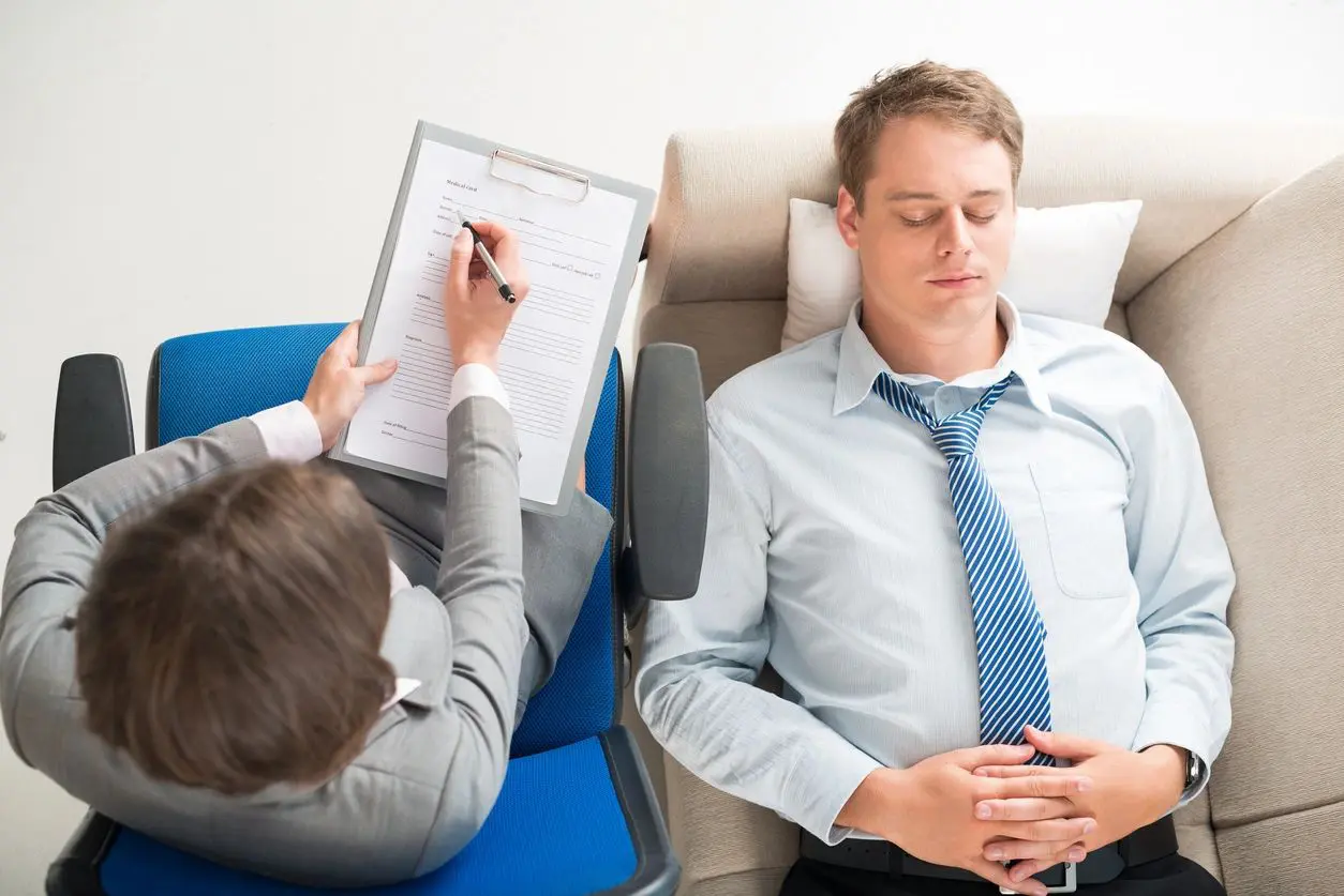 A man sitting in front of another man while writing on paper.